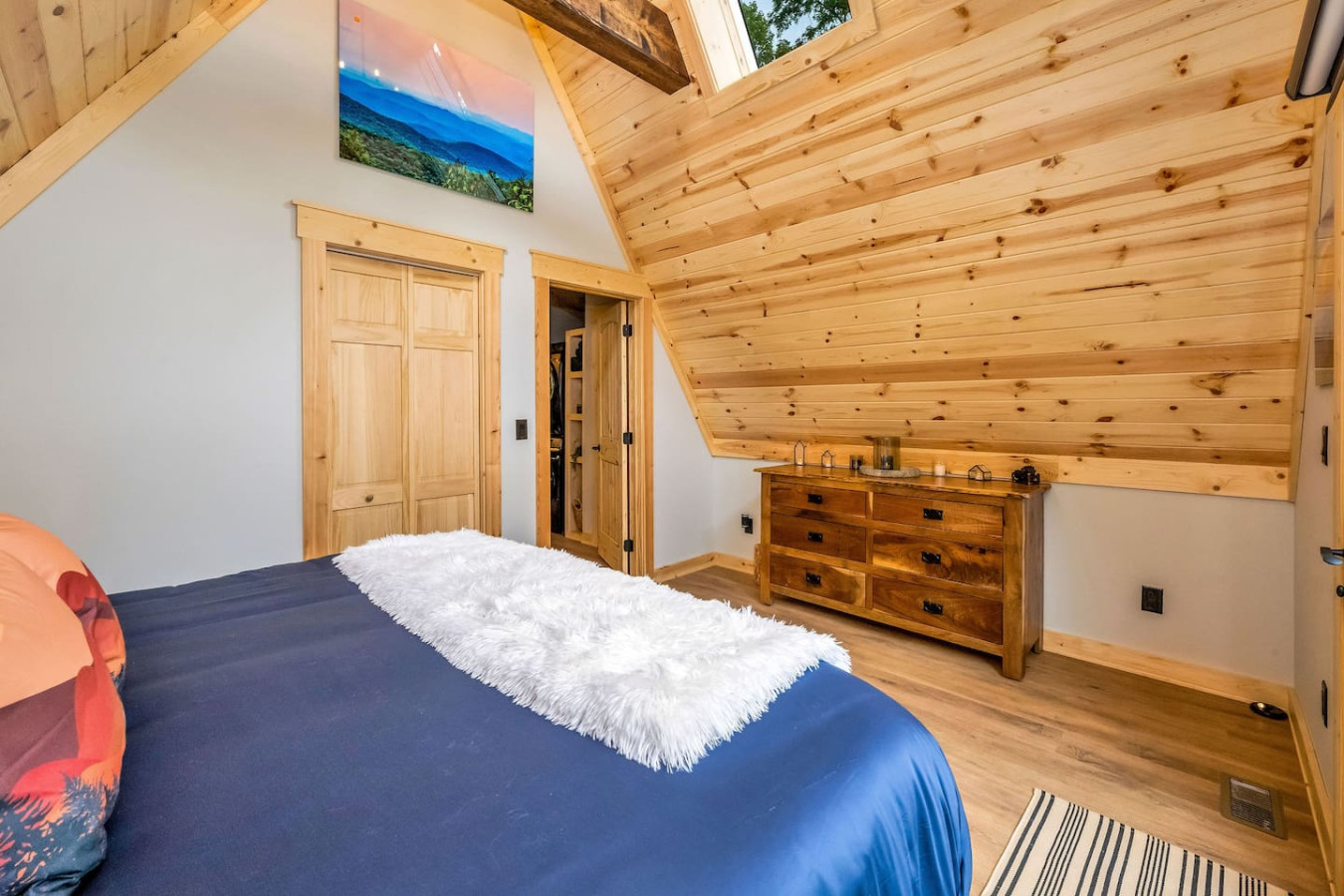 King bedroom with navy bedding, skylight, and wood-plank A-frame ceiling