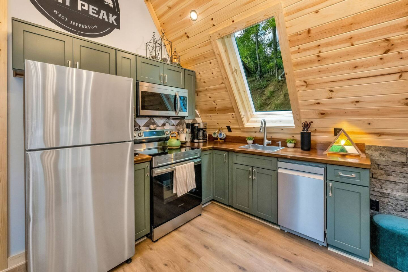 Sage-green kitchen under the A-frame skylight with High Peak logo