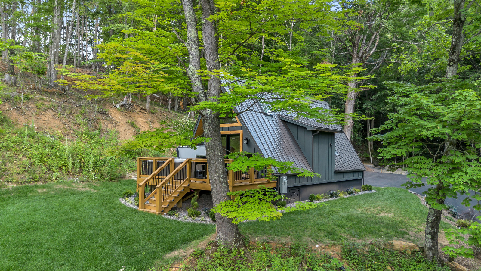 High Peak A-frame on the wooded hillside with deck, hot tub, and lawn